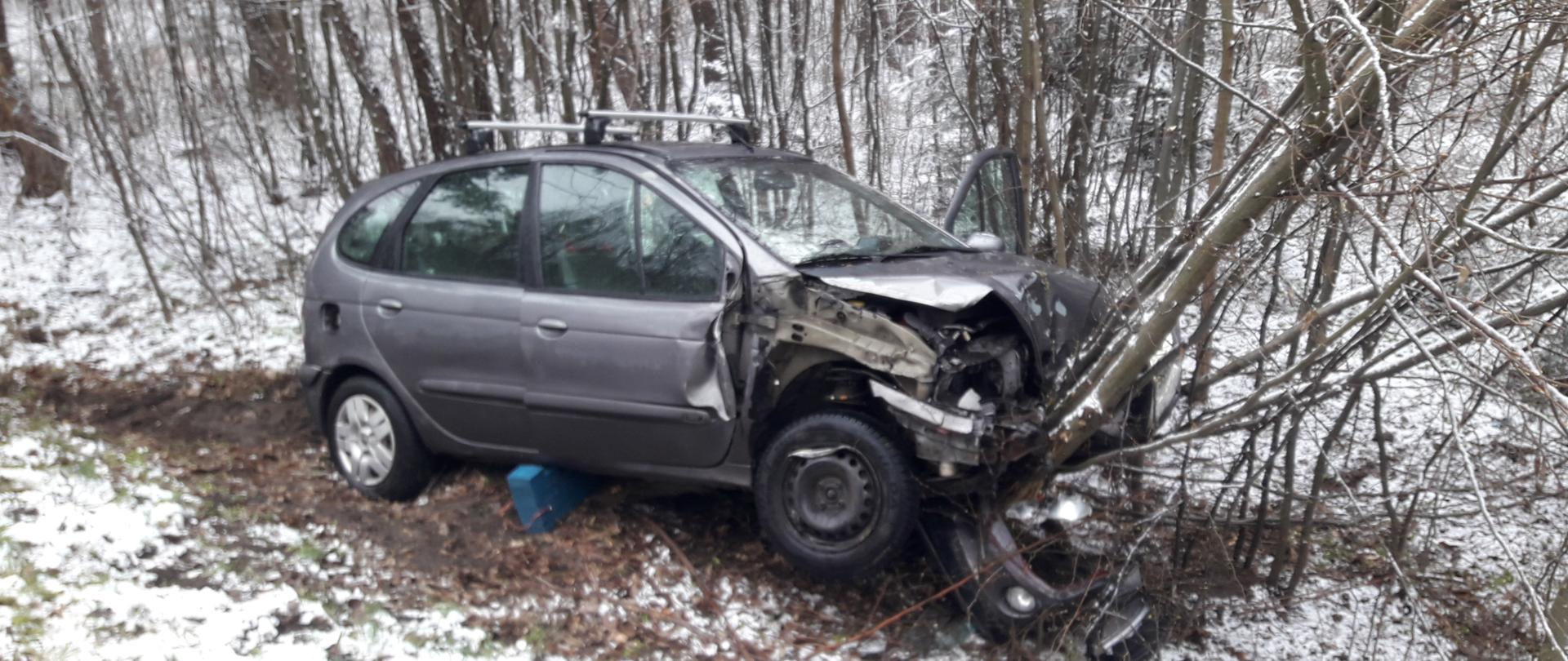 Zdjęcie przedstawia uszkodzony w wyniku zderzenia samochód osobowy marki Renault Scenic, który znajduje się poza jezdnią w przydrożnym rowie.