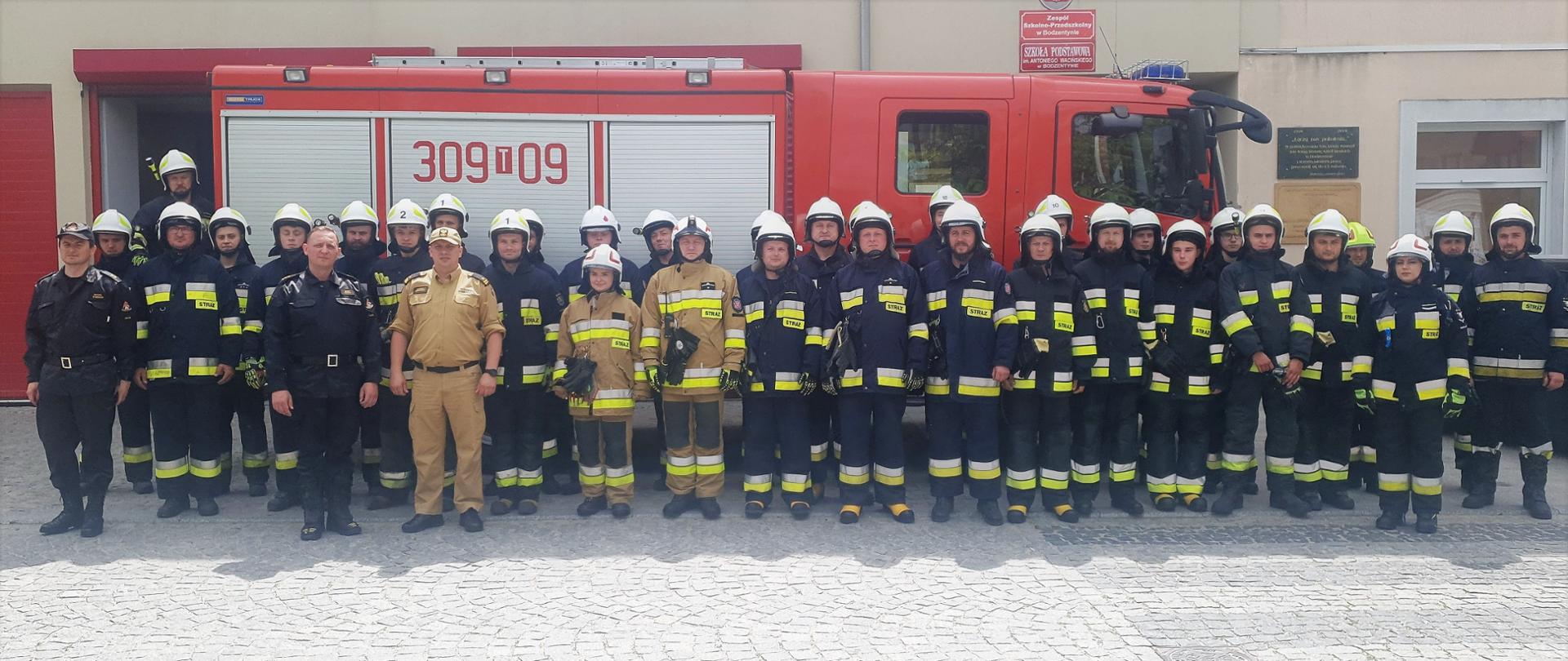 Na zdjęciu przedstawiono grupę druhów, który brali udział w szkoleniu podstawowym wraz z instruktorami z komendy miejskiej straży pożarnej w Kielcach na tle samochodu pożarniczego. 
