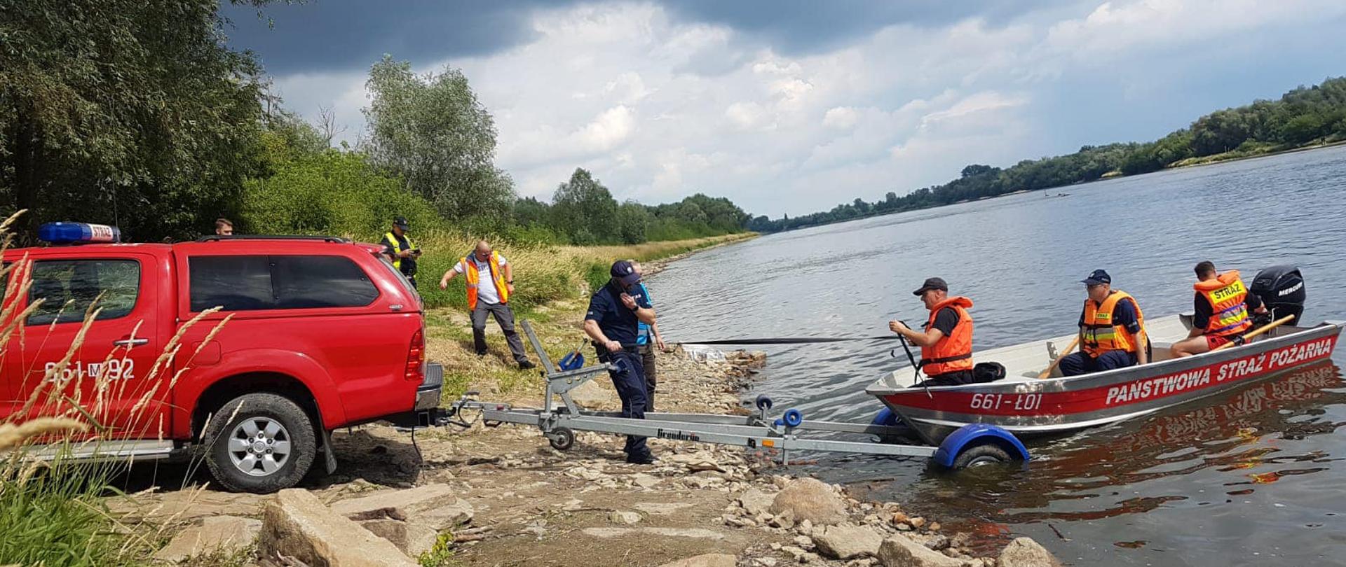 Strażacy wyciągają łódź z wody na przyczepkę po łodziową podpiętą do samochodu 