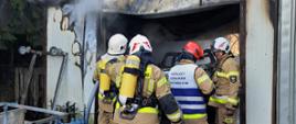 Zdjęcie przedstawia strażaków w trakcie prowadzenia rozpoznania pożaru samochodu w pomieszczeniu lakierni