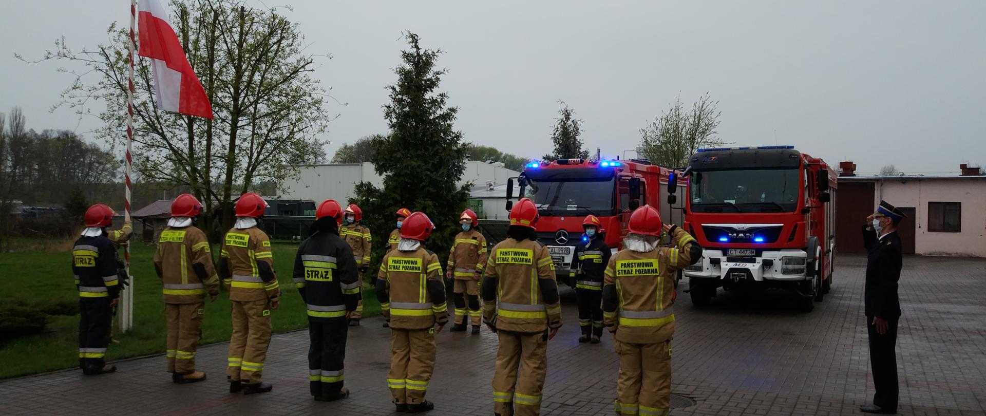 Zmiany służy w Jednostce Ratowniczo Gaśniczej w Aleksandrow Kujawskim połączona z uroczystym podniesieniem flagi państwowej na maszt z okazji Święta Flagi.
Na zdjęci widoczni strażacy stojący w dwóch rzędach prostopadle do masztu flagowego w pełnym ubraniu specjalnym ( żółte ubrania ochronne , czerwone hełmy). W tle widoczne pojazdy pożarnicze z włączonymi światłami błyskowymi stojące na placu jednostki.
Dowódcy zmian służbowych (stojący pierwsi od strony maszt) oddają honor patrząc na podnoszoną flagę. Na wprost masztu stoi funkcjonariusz ubrany w mundur wyjściowy Państwowej Straży Pożarnej także oddający honor, wpatrzony w podnoszoną flagę państwową. Jest to zastępca komendanta powiatowego biorący udział w uroczystym podniesieniu flagi. Jeden z funkcjonariuszy ubrany w ubranie specjalne i hełm wciąga flagę na maszt, flaga znajduje się w połowie masztu.
