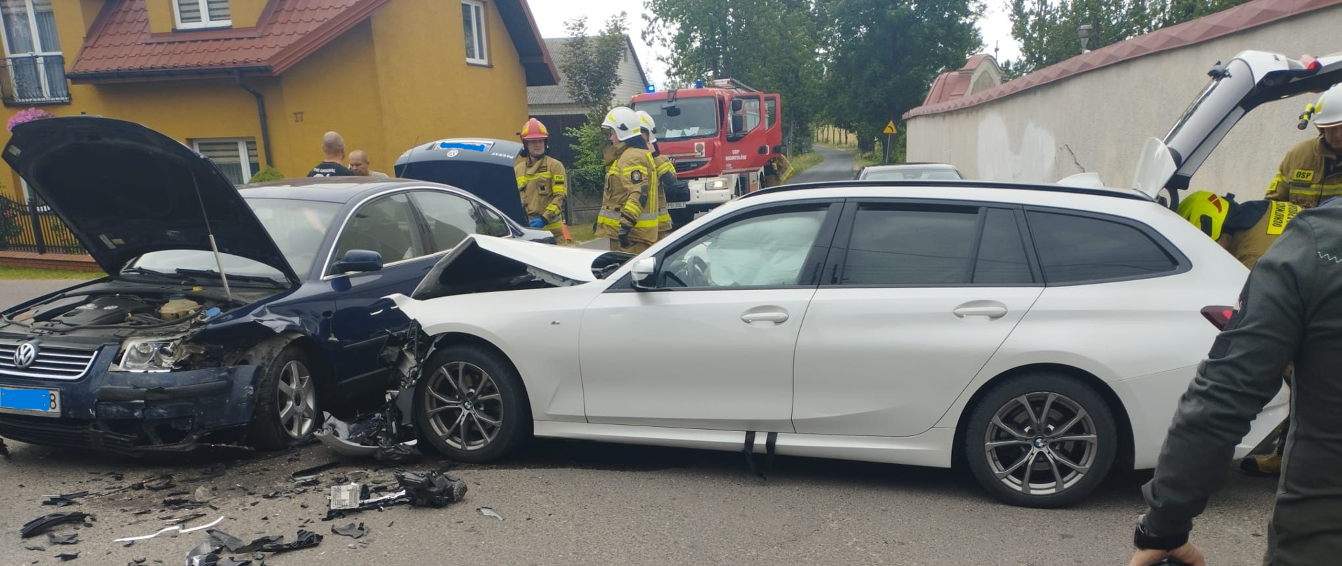 biały samochód uderzył w bok granatowego samochodu w tle widać wóz strażacki przy samochodzie stoi trzech strażaków