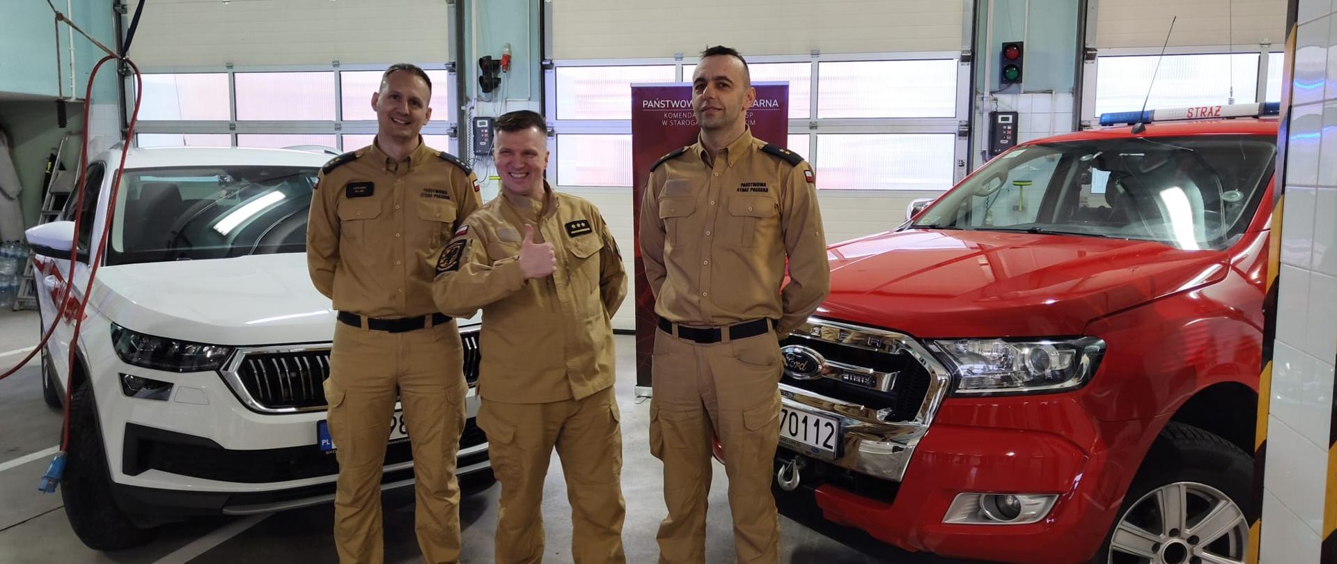 Zdjęcie przedstawia odchodzącego strażaka w towarzystwie dowódców JRG, w tle samochody pożarnicze