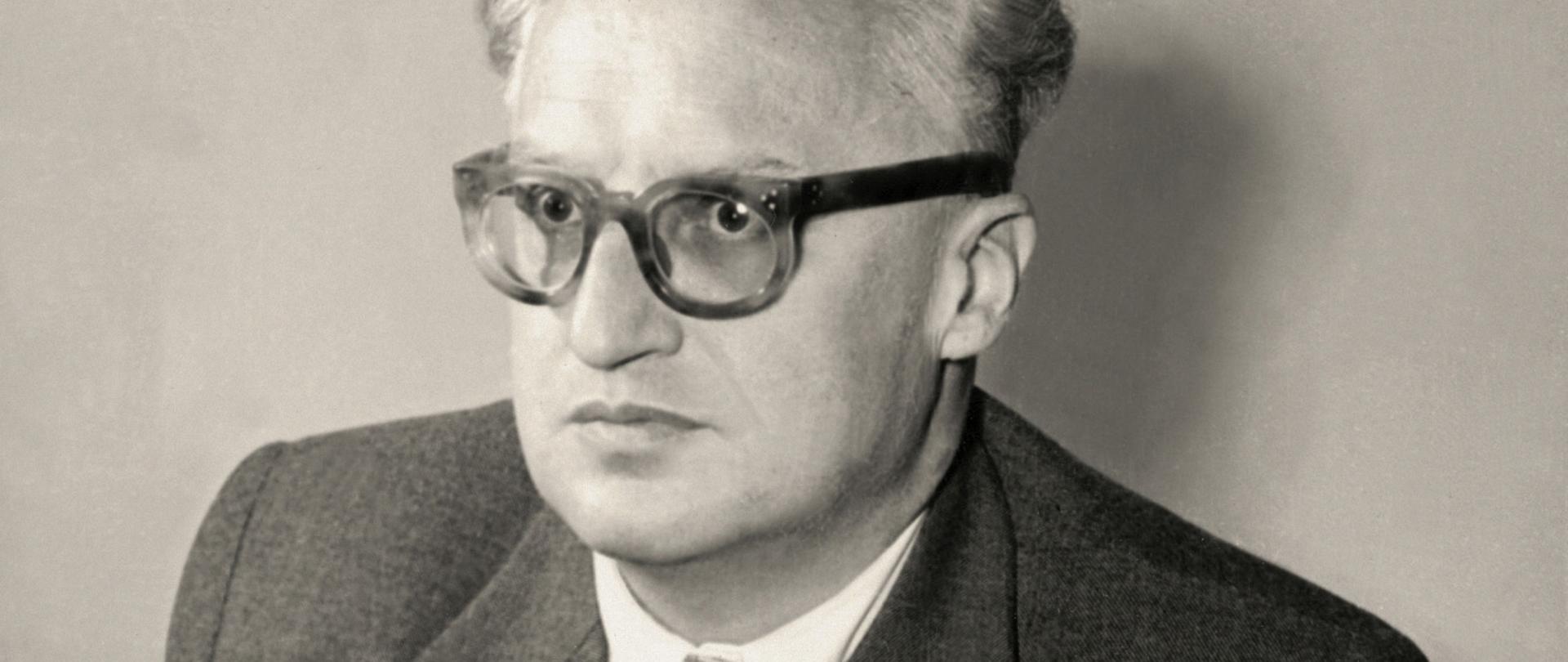 Stanisław Skrzeszewski - czarno-biały portret mężczyzny w okularach z grubymi oprawkami, siwe włosy, ciemna marynarka, jasny krawat w drobne ciemne wzory, kamizelka.