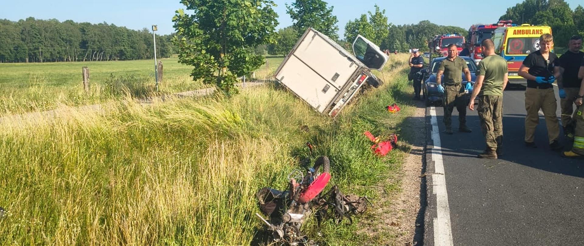 Zderzenie busa z motorowerem, bus w rowie, wrak motoroweru w rowie, liczne służby w tle.