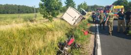 Zderzenie busa z motorowerem, bus w rowie, wrak motoroweru w rowie, liczne służby w tle.