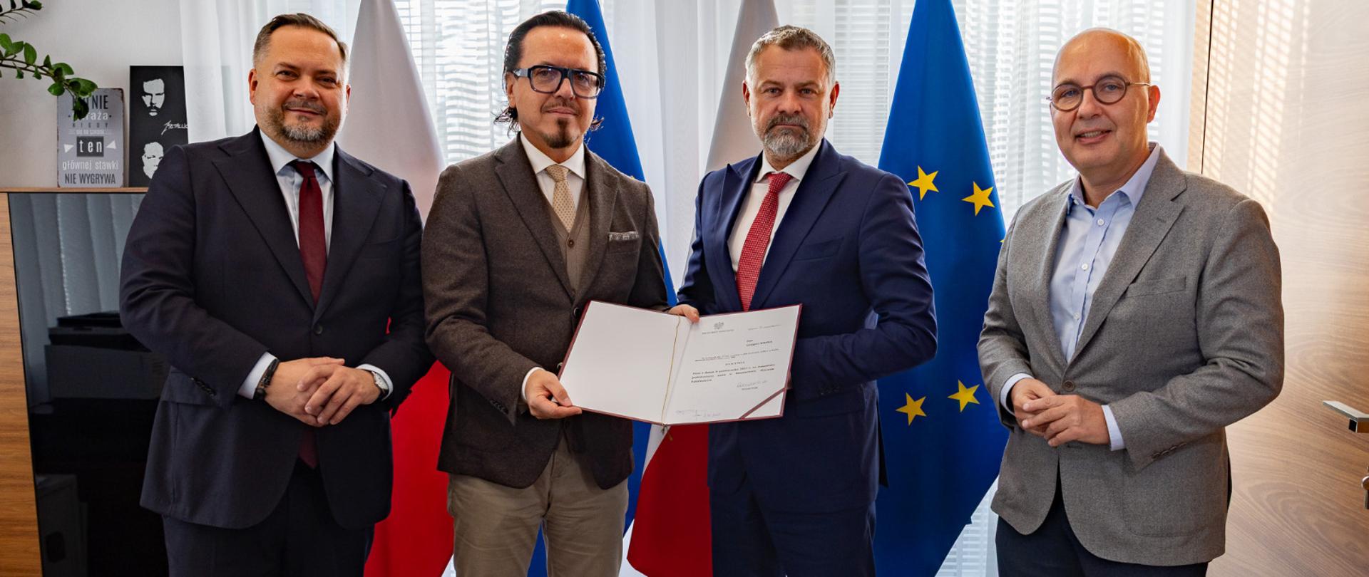 Od lewej: wiceminister Konrad Gołota, minister Wojciech Balczun, wiceminister Grzegorz Wrona, wiceminister Robert Kropiwnicki. W tle flagi. 