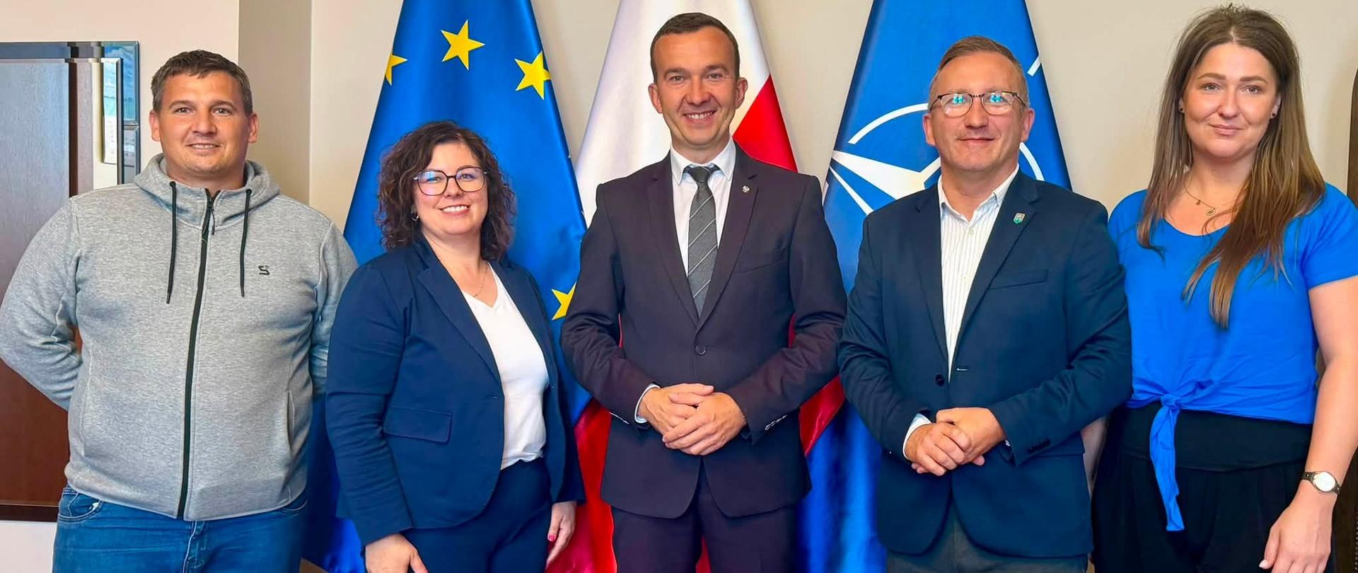 pięć osób stoi na tle flag - flagi Polski, Unii Europejskiej i Nato.
