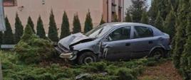 Zdjęcie przedstawia samochód osobowy ze zniszczonym przodem znajdujący się na posesji na którą wjechał po wypadku.