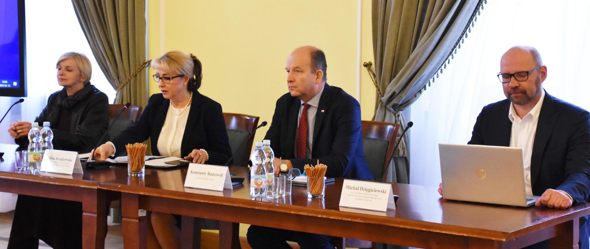 Stół prezydialny, przy którym siedzą cztery osoby. 