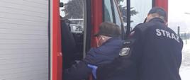 Zdjęcie przedstawia strażaka, który pomaga starszemu mężczyźnie wejść do samochodu strażackiego 