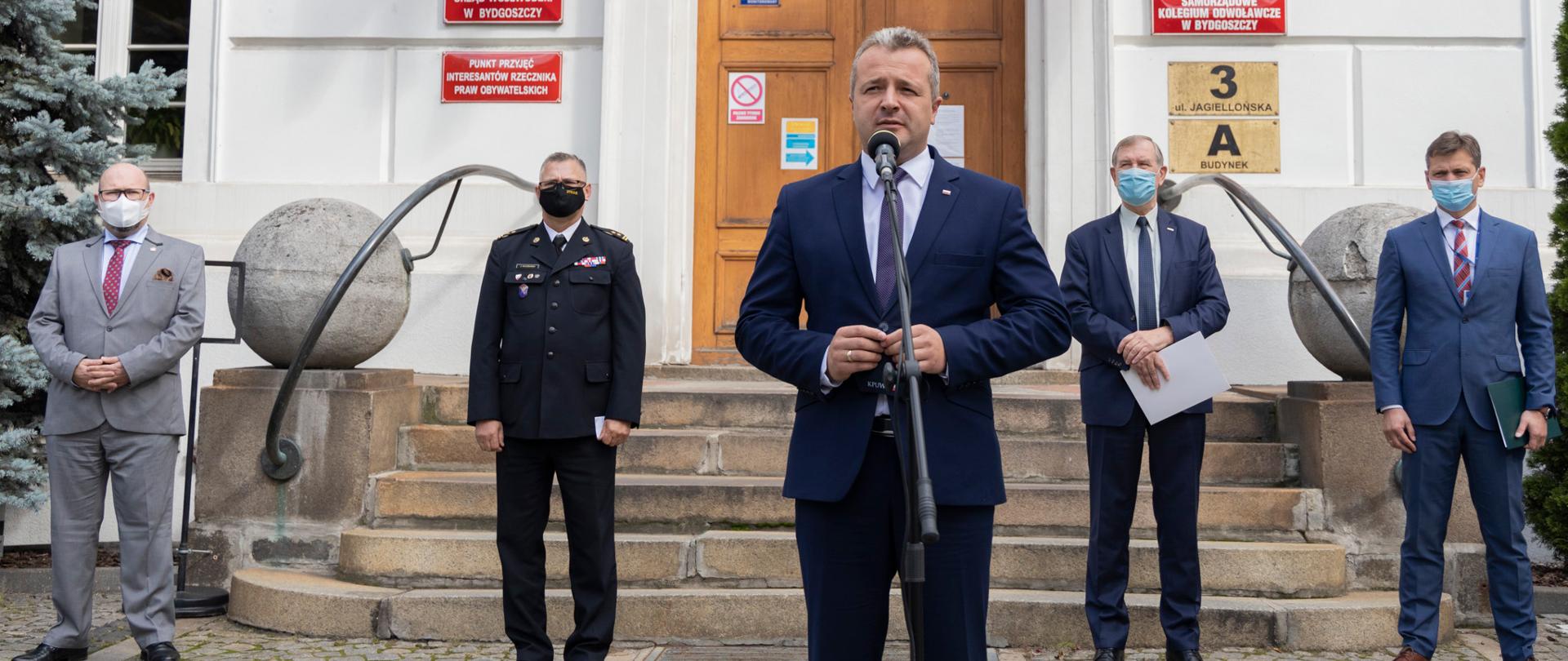 Mężczyźni w garniturach i mundurach w maseczkach przed budynkiem KPUW. Na pierwszym planie wojewoda Mikołaj Bogdanowicz