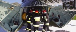Zdjęcie przedstawia strażaków Wojskowej Straży Pożarnej ewakuujących poszkodowanych ze śmigłowca.