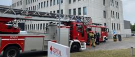 Na zdjęciach widać samochody pożarnicze przed budynkiem szpitala. Obok pojazdów strażacy ubierają aparaty ochrony dróg oddechowych i zabierają niezbędny sprzęt