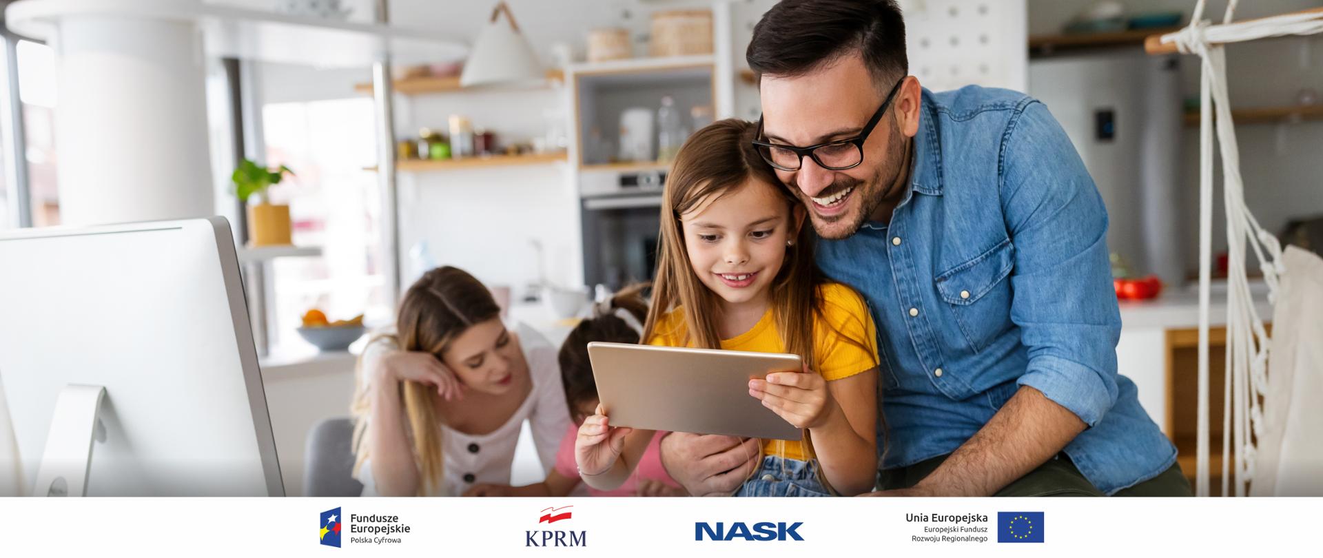 Zdjęcie rodziców i córek. Na pierwszym planie tata obejmujący córkę korzystającą z tableta. W tle mama przed komputerem, z drugą z dziewczynek.