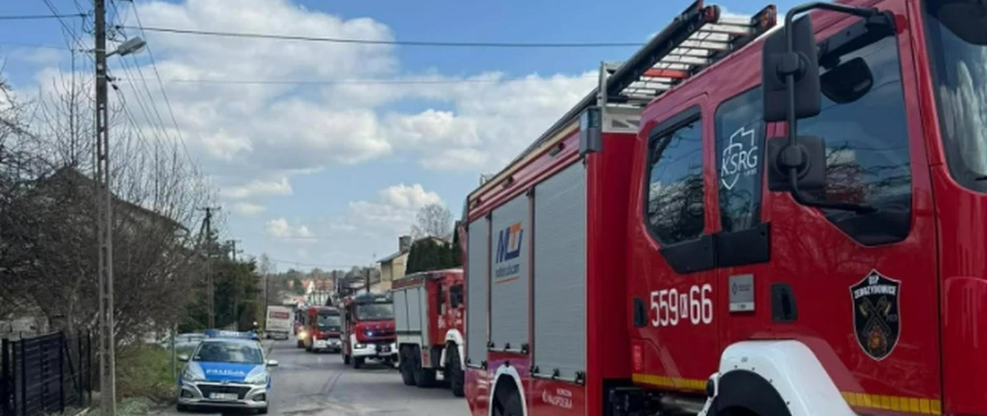 Na zdjęciu widać kolumnę aut strażackich ustawionych na drodze oraz samochód policyjny.