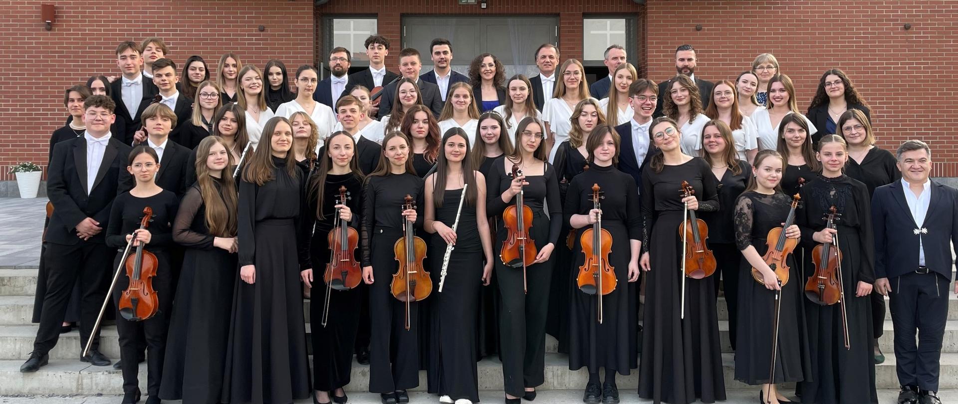 grupowe zdjęcie orkiestry symfonicznej PSM II stopnia w Mielcu na tle kościoła w Woli Mieleckiej