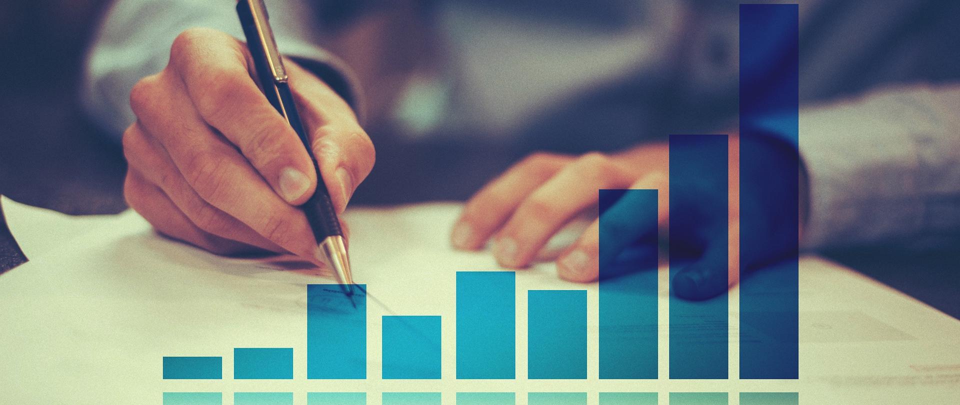 Zdjęcie w poziomie. Niebieski wykres. W tle mężczyzna piszący w notesie