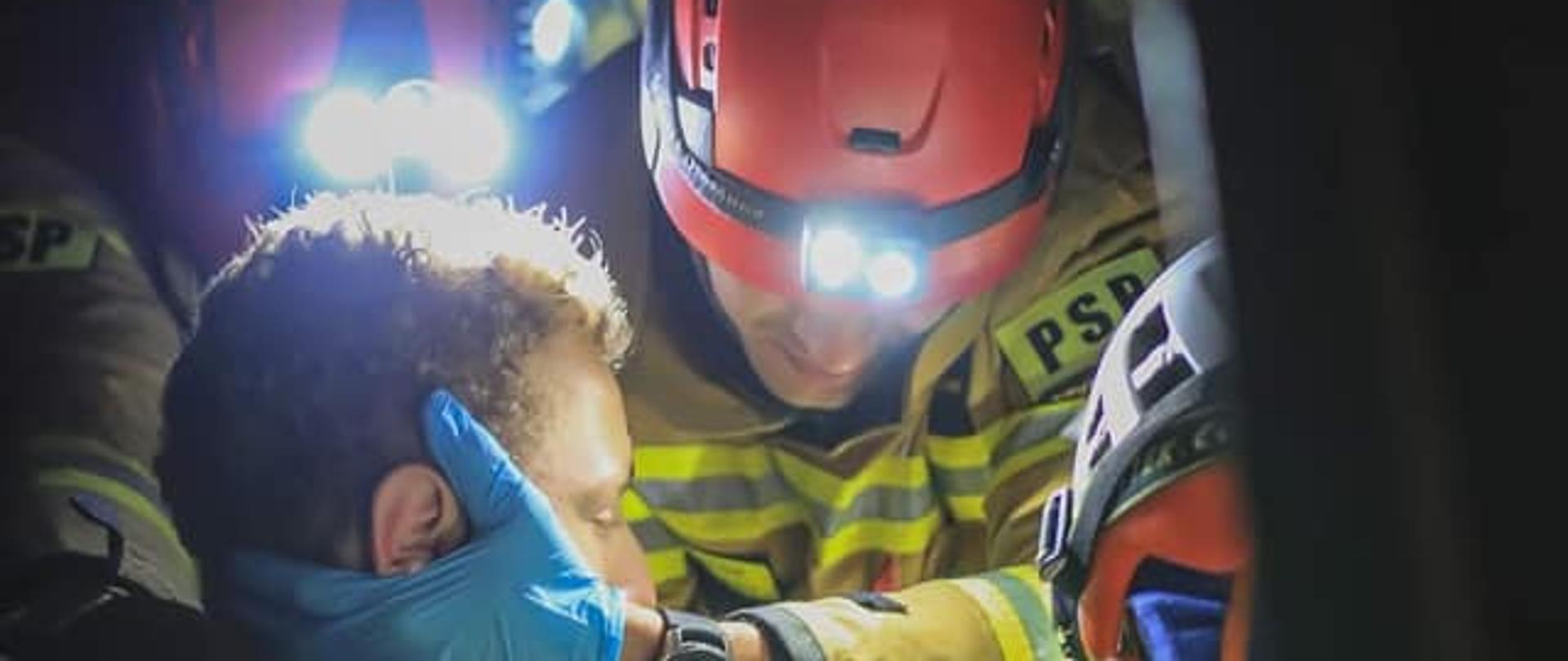 Na zdjęciu widać strażaka udzielającego pomocy osobie poszkodowanej. Osoba jest w pojeździe. 