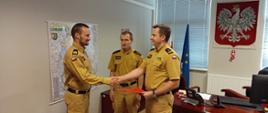 Fotografia przedstawia Komendanta Powiatowego Państwowej Straży Pożarnej w Strzelcach Krajeńskich wręczającego w gabinecie decyzję o przyznaniu nagrody funkcjonariuszowi z Jednostki Ratowniczo-Gaśniczej PSP w Strzelcach Krajeńskich.