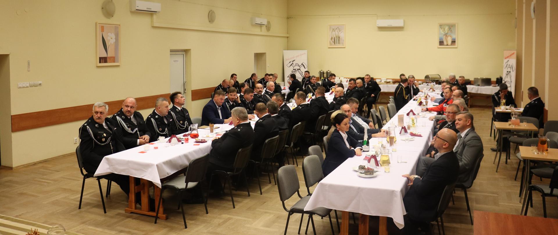 Zdjęcie ukazuje wszystkie osoby uczestniczące w zebraniu. Osoby siedzą przy stołach. Zdjęcie wykonane wewnątrz budynku. 