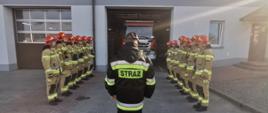 Zdjęcie przestawia strażaków stojących w dwuszeregu przed remizą PSP.