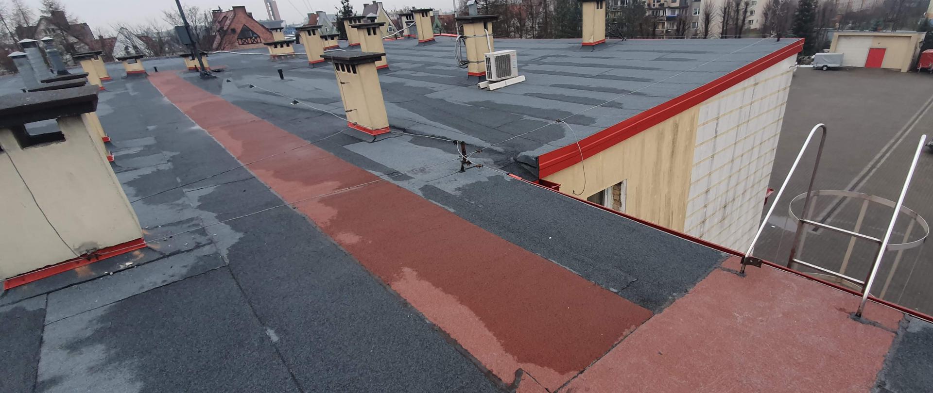 Dach budynku Komendy Powiatowej PSP w Chojnicach, ukazujące powierzchnie pokrycia dachu z papy termozgrzewalnej, widoczne kominy i instalacje znajdujące się na dachu. 