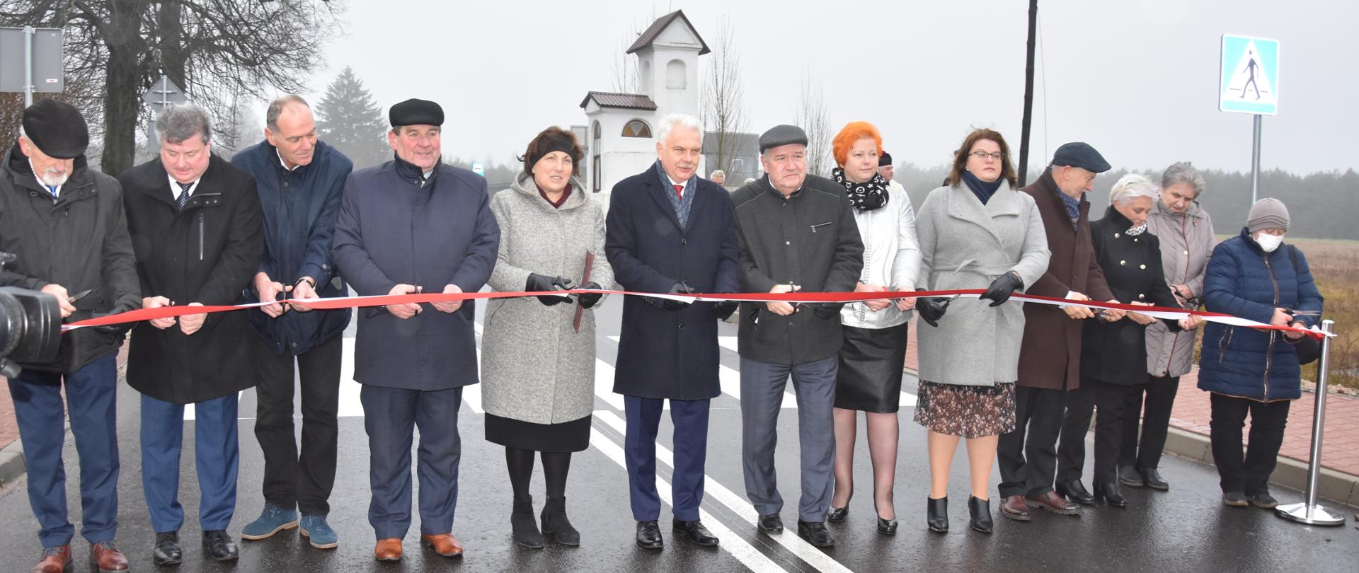 Na zdjęciu znajduje się trzynaście osób, które przecinają wstęgę 
