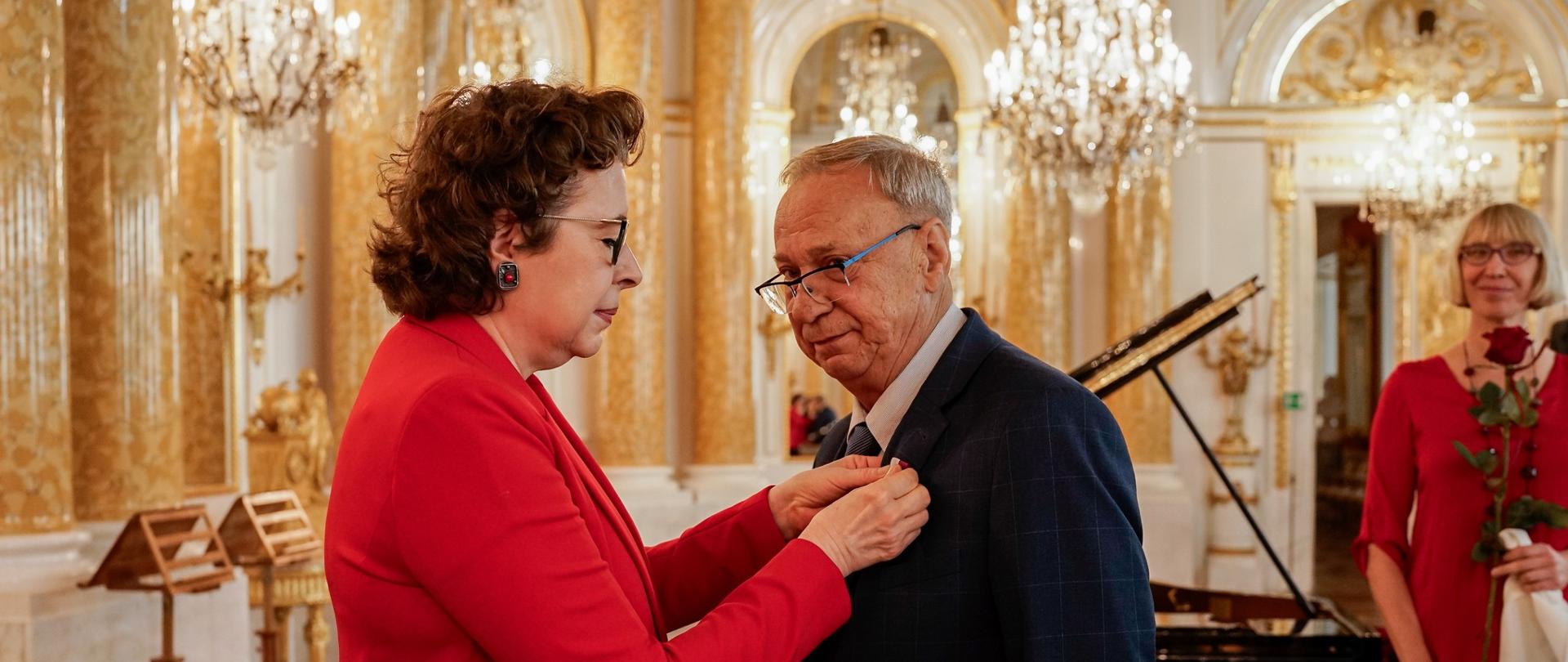 Kobieta przypina mężczyźnie do klapy marynarki medal