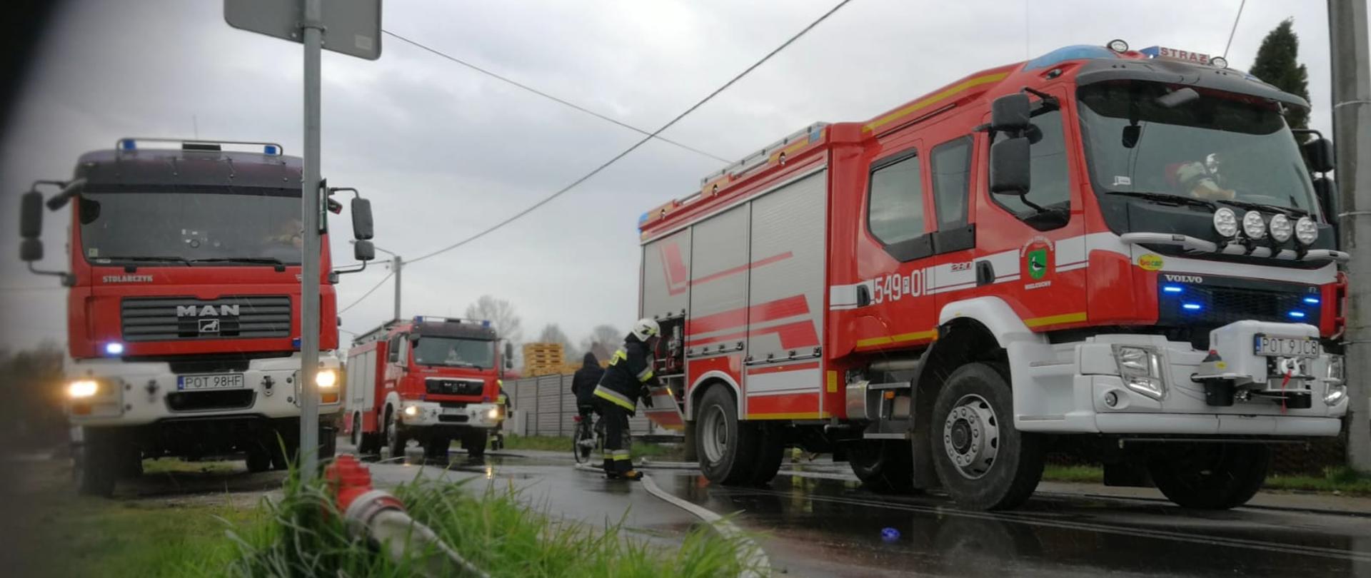 Zdjęcie przedstawia akcję ratowniczo- gaśniczą pożaru budynku garażowo - produkcyjnego.
Na zdjęciu widać 3 pojazdy ratowniczo - gaśnicze biorące udział w akcji oraz strażaka obsugującego autopompę. Zdjęcie wykonane w porze dziennej na drodze.