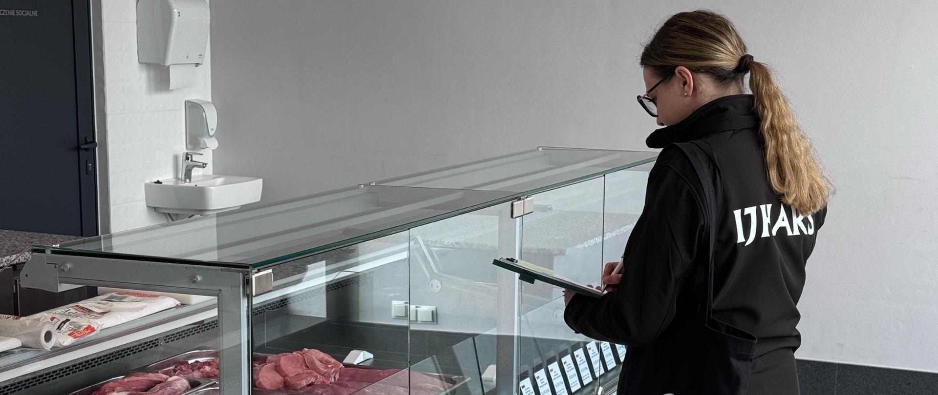 Kobieta stojąca przy ladzie z mięsem, przeprowadza kontrolę