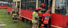 Zdjęcie ukazuję strażaków i ratowników medycznych podczas ewakuacji osoby poszkodowanej przy użyciu noszy typu "deska" z wnętrza pojazdu szynowego.