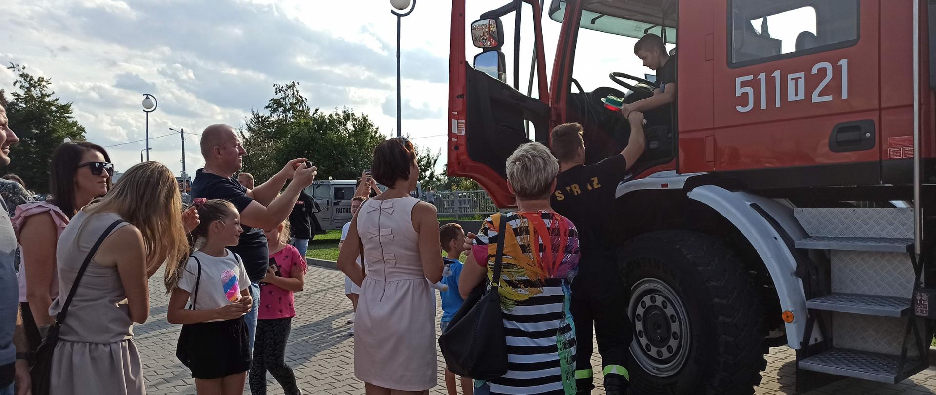 Uczestnicy zlotu stojący przed pojazdem pożarniczym, wykonują zdjęcia osób zasiadających w kabinie pojazdu