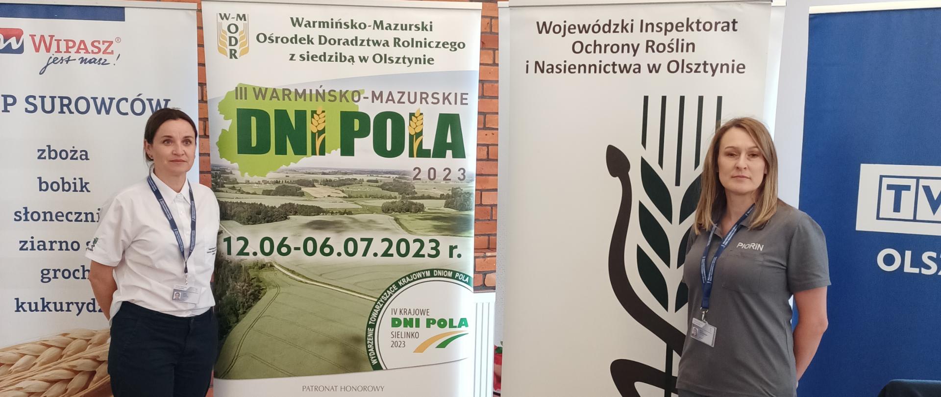 Dwie kobiety w służbowych ubraniach na tle banerów reklamowych instytucji