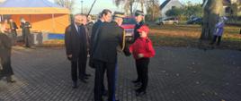 Pomorski komendant wojewódzki Państwowej Straży Pożarnej podaje dłoń przedstawicielowi Młodzieżowej Drużyny Pożarniczej obok stoją zaproszeni goście oraz członek ochotniczej straży pożarnej.