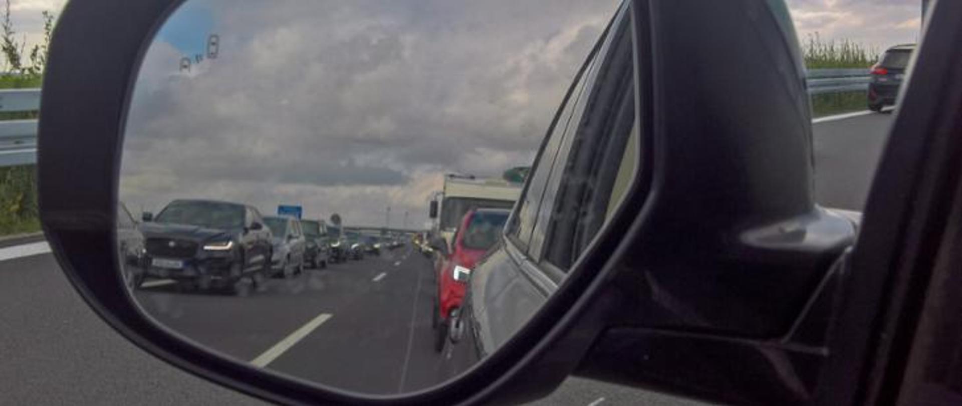 Korytarz życia, zdjęcie lusterka samochodowego, w którym widoczny jest korytarz życia na drodze dwupasmowej