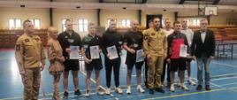 Na zdjęciu generał PSP pozuje do zdjęcia ze zwycięzcami. Wydarzenie w hali sportowej. Generał w mundurze a sportowcy w odzieży sportowej.