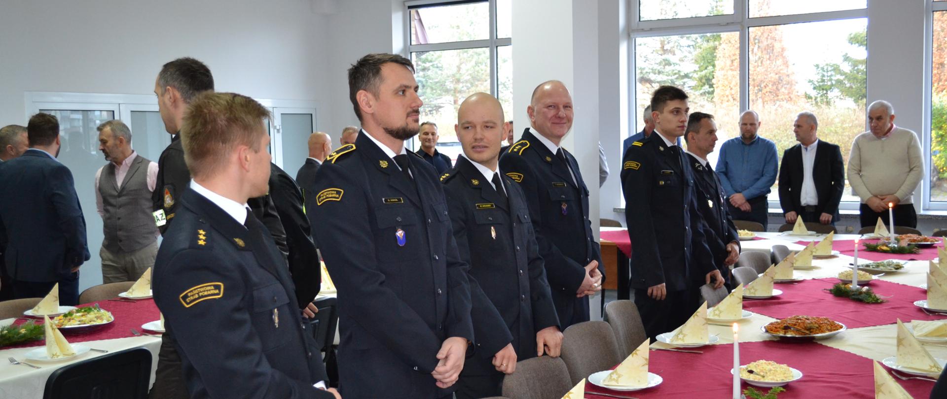 Strażacy i zaproszeni stoją przy stołach