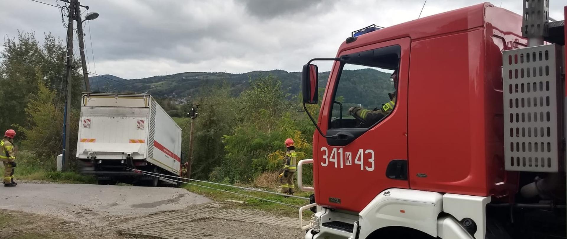 Samochód ciężarowy poza drogą oraz fragment samochodu pożarniczego.
