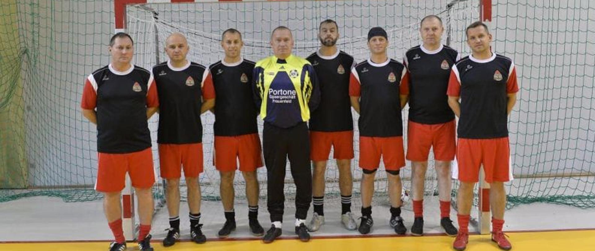 Zdjęcie grupowe drużyny. Zawodnicy stoją w szeregu, przed bramką na hali sportowej. Wszyscy w strojach reprezentacji województwa. Na środku bramkarz.