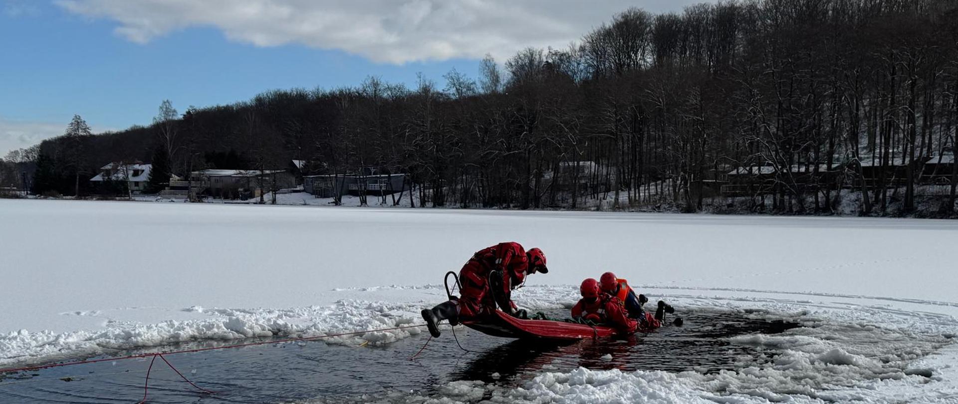 Na zdjęciu strażacy podbierają pozoranta z przerębla na sanie lodowe.