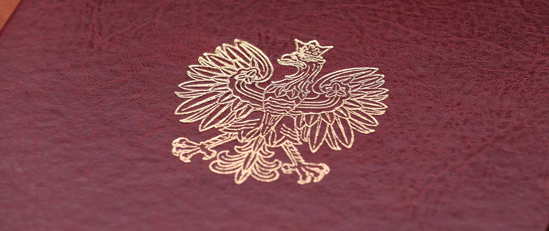 Na zdjęciu widać fragment twardej oprawy na dokumenty z wytłoczonym orłem z godła narodowego.