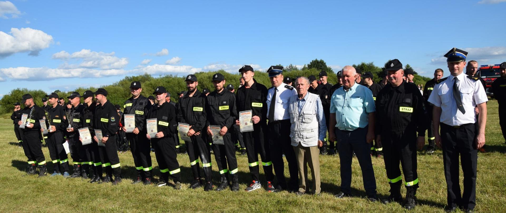 Gminne Zawody Sportowo – Pożarnicze jednostek OSP z terenu gminy Jabłonna Lacka 2022 - na zdjęciu strażacy w ubraniu koszarowym i wyjściowym stoją na zbiórce na boisku trawiastym.