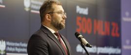 Minister funduszy i polityki regionalnej Grzegorz Puda stoi przy mikrofonie i przemawia, za jego plecami baner MFiPR z napisem o wsparciu 500 mln zł dla przedsiębiorców