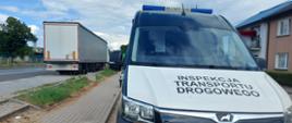 Na pierwszym planie: przód oznakowanego furgonu mazowieckiej Inspekcji Transportu Drogowego. W tle: kontrolowany ciągnik siodłowy z podpiętą naczepą stoi w zatoce przy drodze krajowej numer 50.