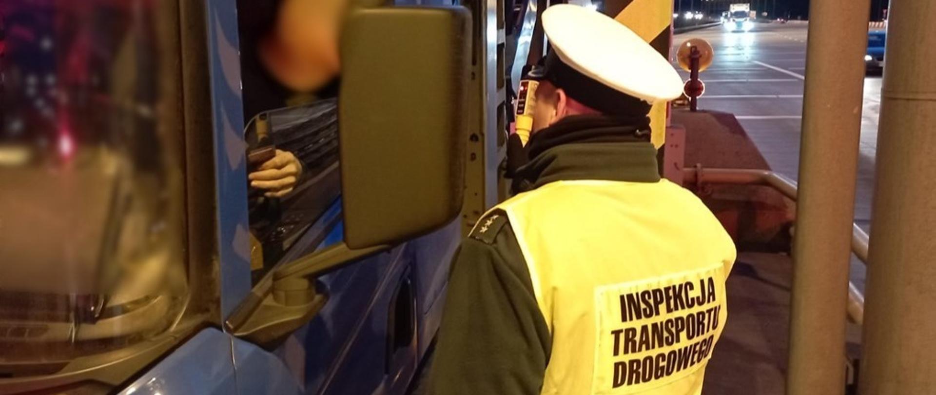 Umundurowany funkcjonariusz lubuskiej Inspekcji Transportu Drogowego stoi obok drzwi kabiny ciężarówki i kontroluje trzeźwość kierowcy. Inspektor trzyma w ręku alkomat przesiewowy i pokazuje wynik badania kierowcy.