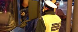 Umundurowany funkcjonariusz lubuskiej Inspekcji Transportu Drogowego stoi obok drzwi kabiny ciężarówki i kontroluje trzeźwość kierowcy. Inspektor trzyma w ręku alkomat przesiewowy i pokazuje wynik badania kierowcy.
