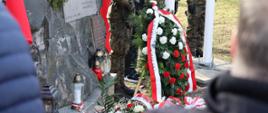 Na zdjęciu znajduje się pomnik Armii Krajowej w Opolu. Obok znajdują się złożone znicze, kwiaty i wieńce, przyozdobione biało-czerwonymi wstążkami. 