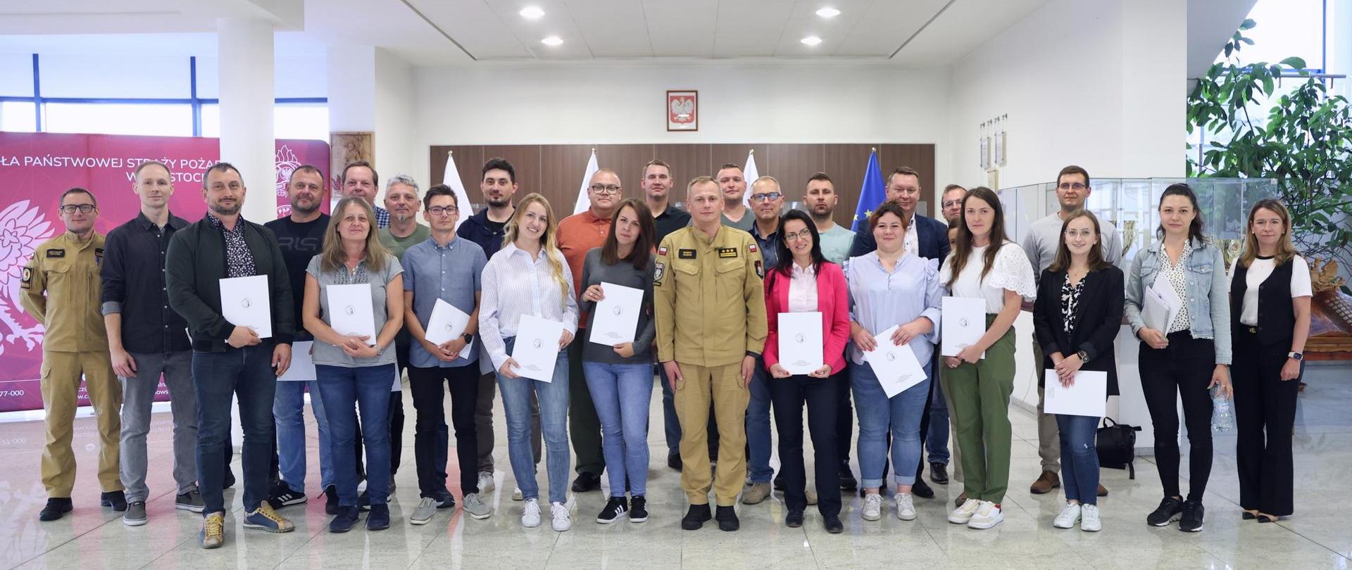 Pamiątkowe zdjęcie grupowe uczestników szkolenia inspektorów ochrony przeciwpożarowej (24 osoby) w towarzystwie Zastępcy Komendanta Centralnej Szkoły PSP, kobiety oraz funkcjonariusza CS PSP