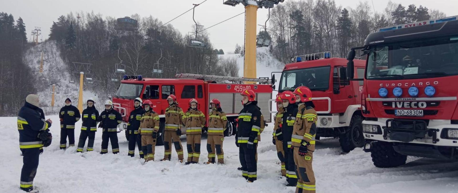 Zdjęcie przedstawia dwunastu strażaków podczas omówienia ćwiczeń związanych z doskonaleniem technik ewakuacji osób poszkodowanych z kolei krzesełkowej przy użyciu drabin przystawnych